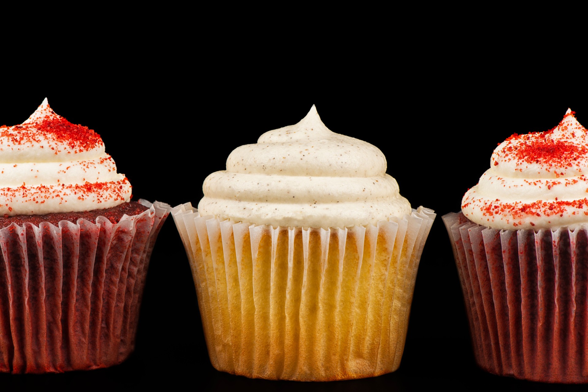 Close-up of three gourmet cupcakes with swirled frosting, including vanilla and red velvet